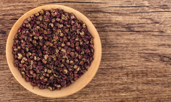 Szechuan pepper in a bowl over wooden background