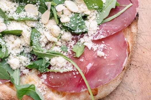 Gourmet pizza with mozzarella, rocket, bresaola, parmesan and almonds. Top view.