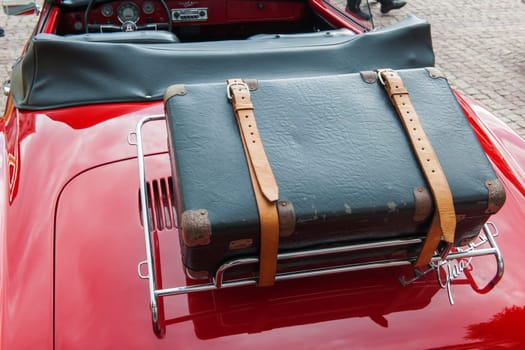 Rear detailed view of a restored red Karmann Ghia convertible with an old black suitcase strapped to the luggage rack.