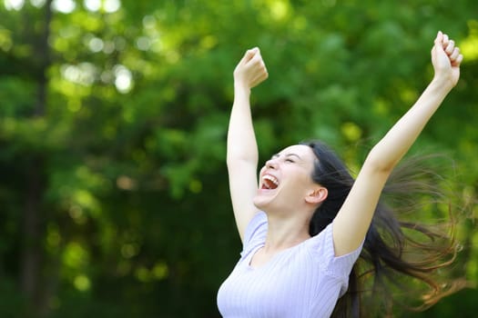 Excited asian woman raising arms in a park