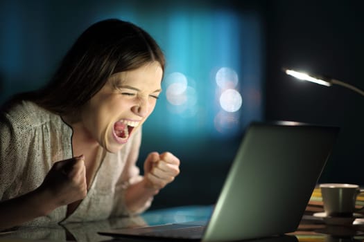 Excited woman checking laptop news in the night