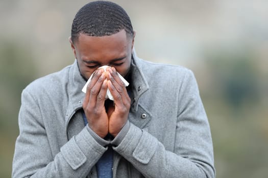 Ill man with black skin blowing on tissue