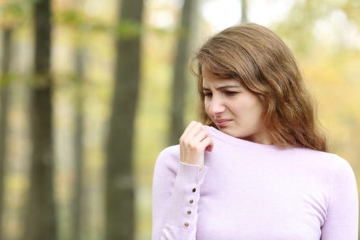Disgusted woman smelling clothes in a forest