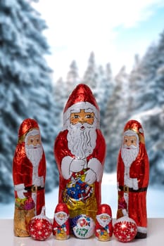 Christmas greeting card. Closeup of various cheerful wrapped chocolate Santa Claus over festive abstract blurred winter landscape. Xmas and New Year gift sweets. Macro.