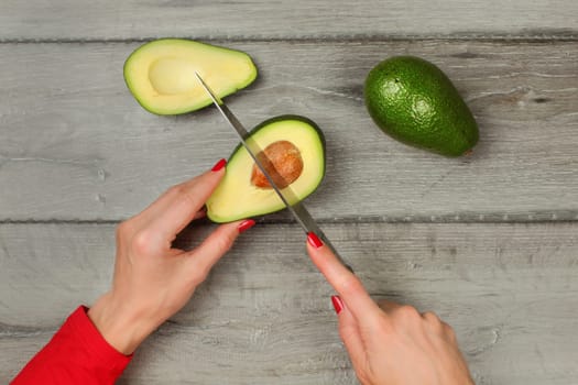 Tabletop view - woman hands holding chef knife, removing seed from avocado cut in half.