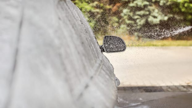 Shampoo foam and water spray falling on side mirror of a car washed in self service carwash. Focus to drops only, left is place for text.