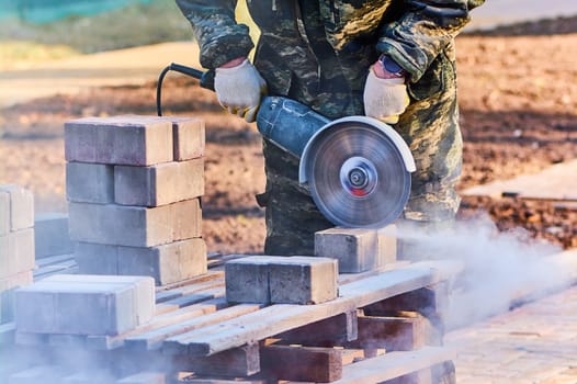 A worker with a circular saw cuts paving slabs in close-up. High quality photo