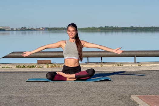 A young woman does a warm-up on the pier in the early morning, against the background of the river. High quality photo