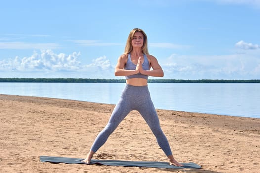 A woman does yoga on a sandy beach against the background of a river. High quality photo