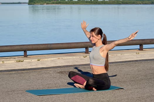 A young woman does a warm-up on the pier in the early morning, against the background of the river. High quality photo