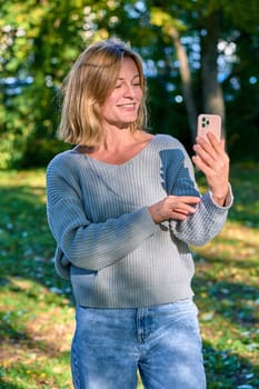 A woman in a park in the summer speaks during a video call on the phone. High quality photo