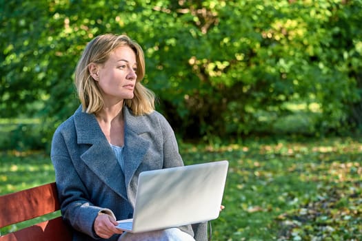 A woman with a laptop is sitting on a park bench. High quality photo