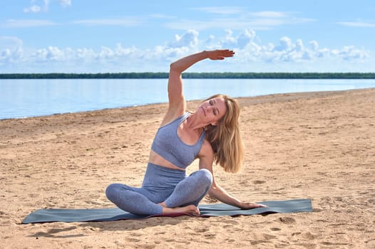 A woman does yoga on a sandy beach against the background of a river. High quality photo
