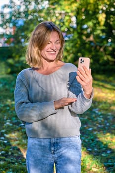 A woman in a park in the summer speaks during a video call on the phone. High quality photo
