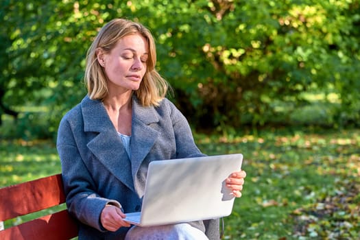 A woman with a laptop is sitting on a park bench. High quality photo