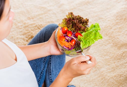 Young woman eating fresh salad meal vegetarian spinach in a bowl, top view of female hands holding bowl with green lettuce salad on legs, Clean detox healthy food concept