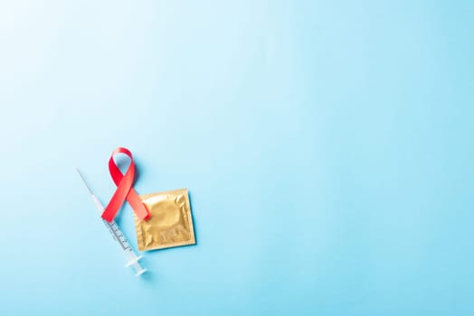 Red bow ribbon symbol HIV, AIDS cancer awareness, condom and syringe with shadows, studio shot isolated on blue background, Healthcare medicine sexually concept, World AIDS Day
