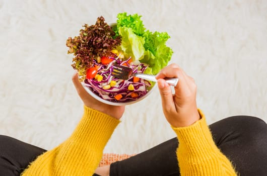 Young woman eating fresh salad meal vegetarian spinach in a bowl, top view of female hands holding bowl with green lettuce salad on legs, Clean detox healthy food concept