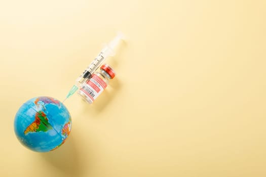 Vaccine vials bottles, syringes for vaccination against coronavirus and globe, medicine illness, COVID-19 disease vaccine isolated on yellow background