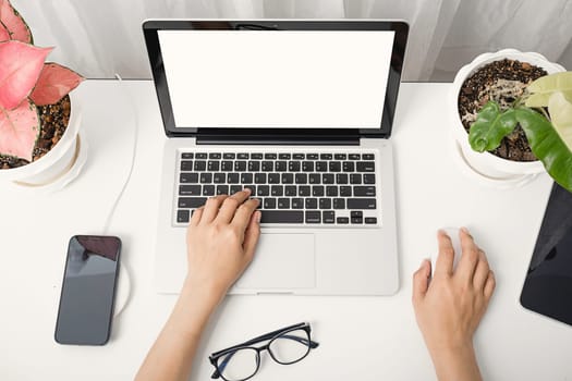 Young Asian woman sitting workspace table she's working on laptop computer blank screen typing keyboard, female using internet on notebook to social media at home office
