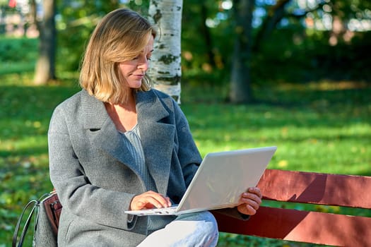 A woman with a laptop is sitting on a park bench on a sunny summer day. High quality photo