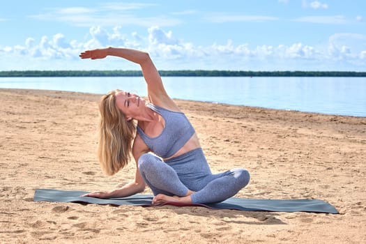 A beautiful woman does yoga on a sandy beach against the background of a river. High quality photo