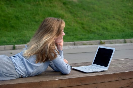 A woman with a laptop lies on a bench and works online. High quality photo