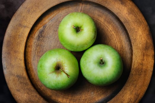 Three green apples in wooden plate