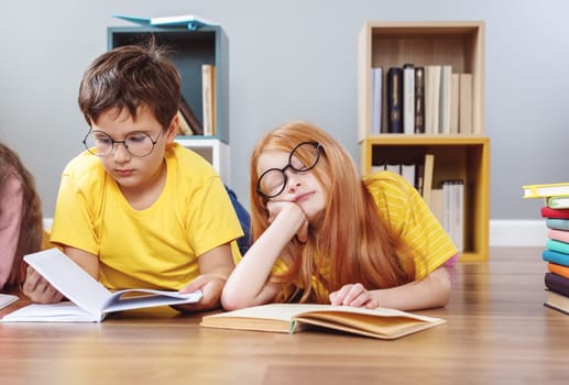 Cute children in glasses lying on the floor indoors with books. Concept of hobby and education.