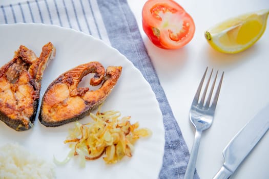 Fried fish with onions, rice and lemon lies on a plate, on a waffle towel and cutlery on a white background. High quality photo