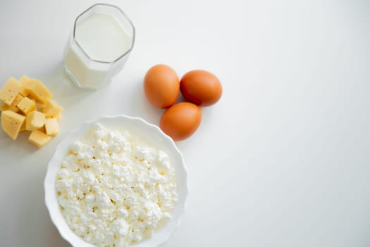 A white bowl with cottage cheese, eggs, diced cheese and a glass of milk stand on a white background. . High quality photo