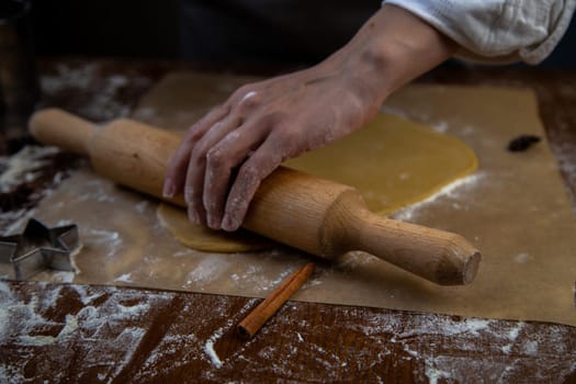 The dough is rolled out with a rolling pin on parchment, flour is scattered around, the photo is in a dark key. High quality photo