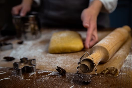 A rectangle of dough lies on baking parchment, a rolling pin and cookie cutters are lying next to it, everything is strewn with flour, a cook is standing in the background and holding a rolling pin and dough with his hand. High quality photo