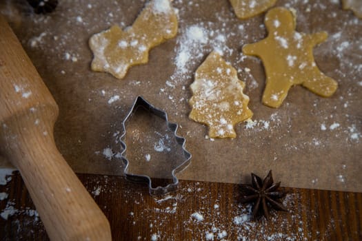 the mold for cookies in the form of Christmas trees on parchment lying next to him are cut from the dough pieces on parchment, next to a rolling pin and all the flour on a dark background. High quality photo