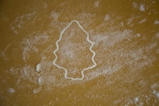 The figure of a Christmas tree is carved on the dough, the contours of which are brightly outlined with flour, the dough is also in flour. High quality photo