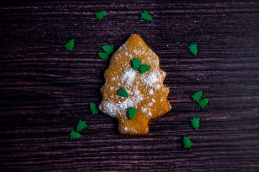 Cookies in the form of a Christmas tree sprinkled on top of white flour and small green Christmas trees on a dark wooden background. High quality photo