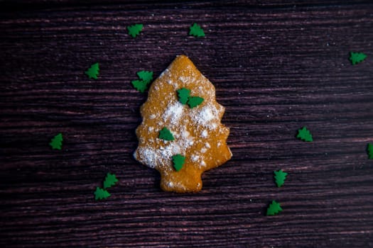 Cookies in the form of a Christmas tree sprinkled on top of white flour and small green Christmas trees on a dark wooden background. High quality photo