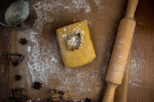 A herringbone-shaped cookie pan rests on the dough and is sprinkled with flour, against the background of a rolling pin, parchment for baking, other molds and flour. High quality photo