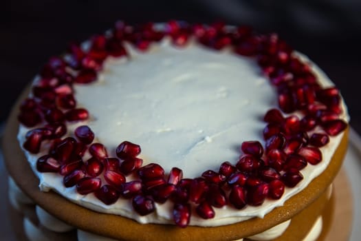 Cake with sponge cakes, decorated with white cream and pomegranate seeds on top in a circle, layers of cream are visible in circles on the side, a close-up view from the side. High quality photo