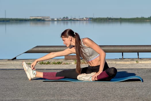A young woman does a warm-up on the pier in the early morning, against the background of the river. High quality photo