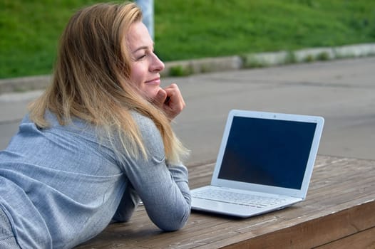 A woman with a laptop lies on a bench and works online. High quality photo