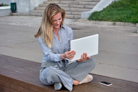 A woman with a laptop sits on a wooden platform, works online. High quality photo
