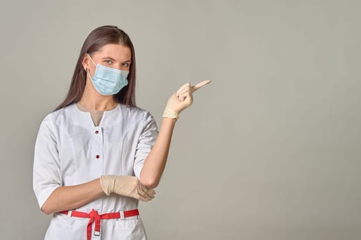 A female doctor in a medical mask points to an empty place, copy space. High quality photo