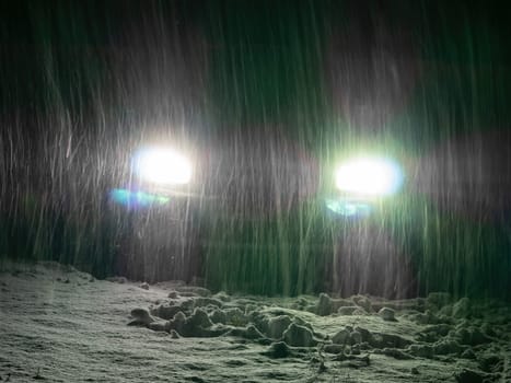 Snow blizzard in the light of car headlights on the night road. Falling white snow. Car headlights. Night automobile road. Winter season. Ice on the track. Frosty weather. Driving in winter.