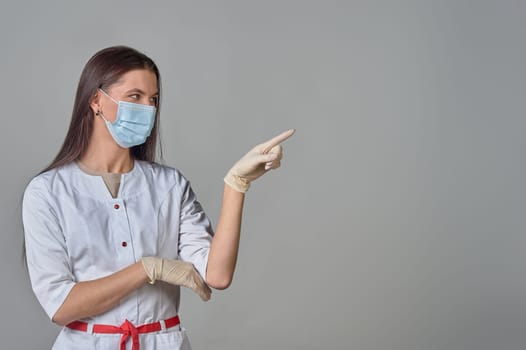 Woman doctor in white coat and medical mask shows copy space. High quality photo
