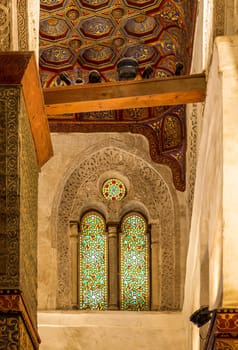 Two adjacent perforated stucco arched windows decorated with colorful stain glass with geometrical and floral patterns, at Mamluk era public historical Qalawun complex, Moez Street, Cairo, Egypt
