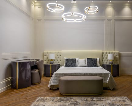 Interior of modern room with comfortable bed and bedside tables with lamps under ceiling with creative chandeliers