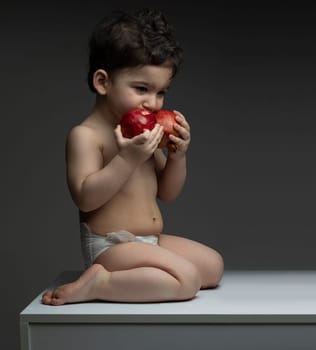 One year old boy with diaper holding two pomegranate in front of mouth