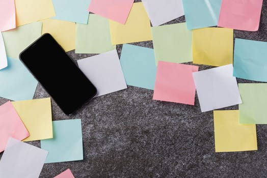 Above many blank paper stick note list with the modern black smart mobile phone blank screen on concrete background, Business smartphone reminder concept