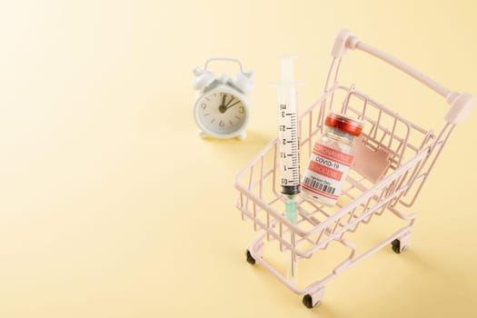 Shopping cart with vaccine vials bottles and syringes for vaccination against coronavirus, medicine illness, COVID-19 disease vaccine studio shot isolated on yellow background